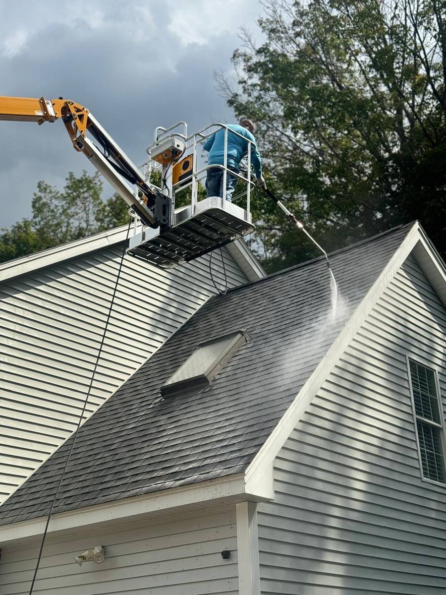 Technician soft washing a roof from the lift basket